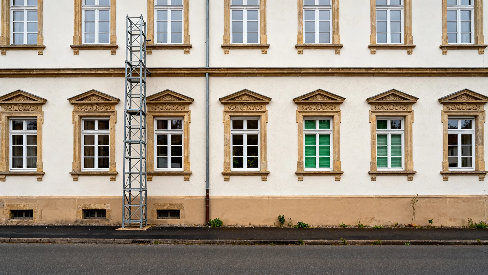 Fassade eines Altbaus mit Sandstein-Fensterrahmungen und einem Gerüstturm an der Wand